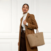 Woman in a brown coat holding a beige handbag against a white background